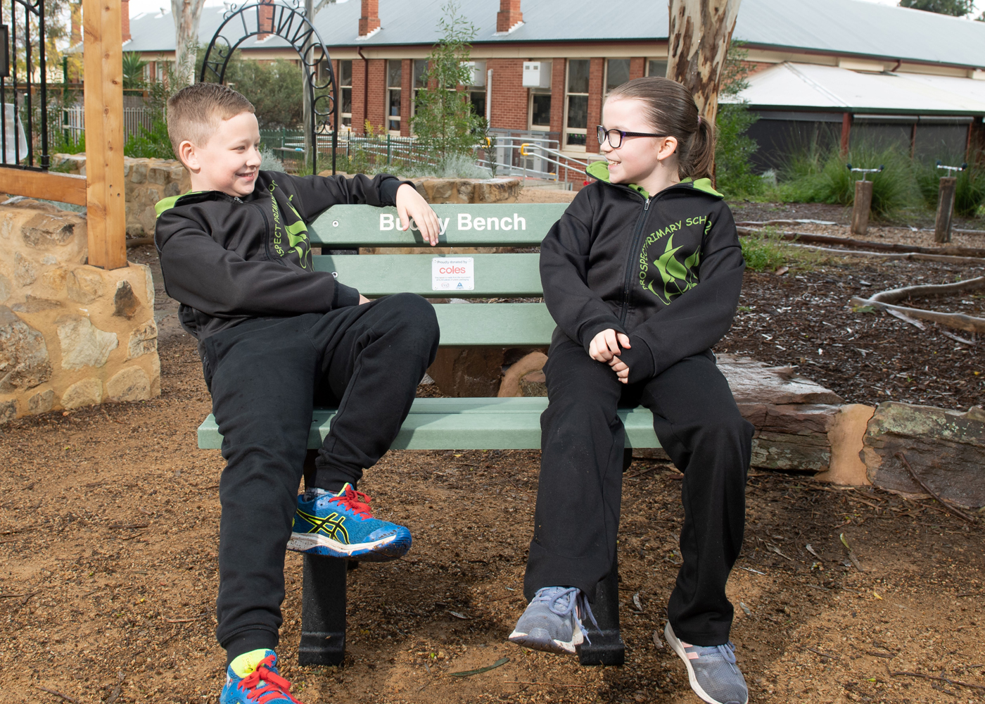 Two Primary School students sitting on an outdoor bench made from 98% recycled plastic